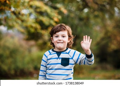 Summer, childhood, leisure, human gesture concept - happy little boy waving hand. Portrait of a little boy in the woods waving his hand. Portrait of a boy. - Powered by Shutterstock