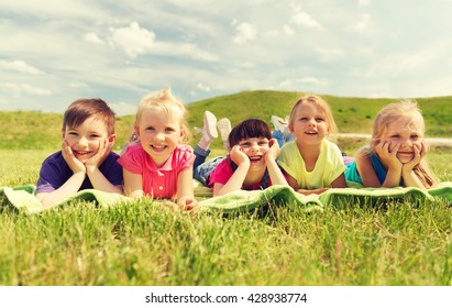 Summer, Childhood, Leisure And People Concept - Group Of Happy Kids Lying On Blanket Or Cover Outdoors