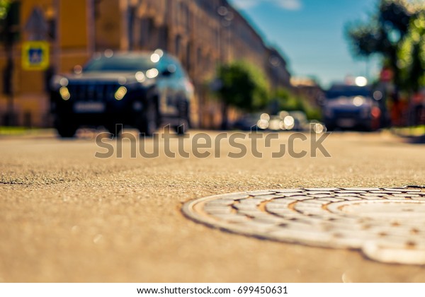 Summer in the city, the car rides down\
the street with trees. Close up view of a hatch at the level of the\
asphalt, image in the yellow-blue\
toning
