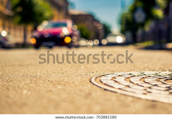 Summer in the city, the\
headlights of an approaching car on the street with trees. Close up\
view of a hatch at the level of the asphalt, image in the\
yellow-blue toning