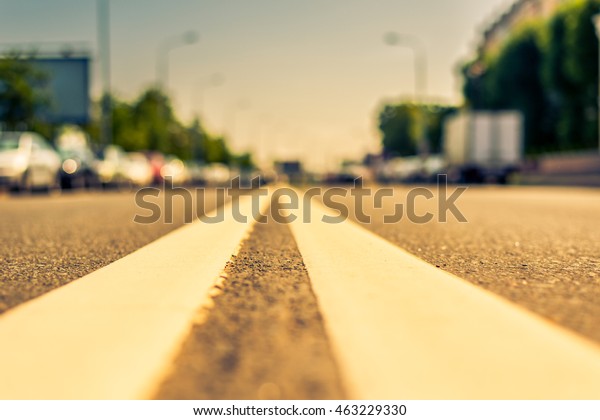 Summer in the city, the street with parked cars.\
Close up view from the level of the double solid line, image in the\
orange-blue toning