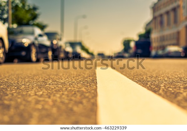 Summer in the city, the street with\
parked cars and traveling on the road. Close up view from the level\
of the dividing line, image in the orange-blue\
toning