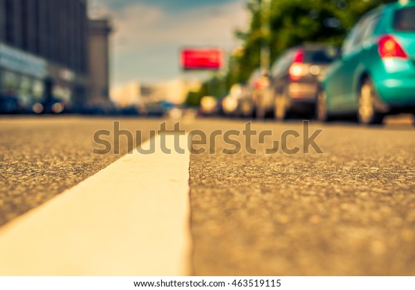 Summer in the city, the street with parked cars.\
Close up view from the level of the dividing line, image in the\
orange-blue toning