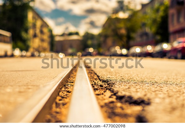 Summer in the city, the street with tramway rails\
and parked cars. Close up view of a tram rail level, image in the\
yellow-blue toning