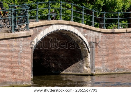 Summer cityscape, Canals of Amsterdam, Under view of brick bridge and railing, Still water and soft sunlight in the afternoon, Canal cruises is very famous activities, Tourist attraction, Netherlands.