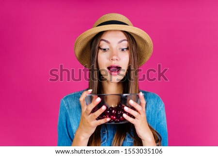 the summer clerk, opening his mouth in surprise, looks into a cup with cherries. background pink