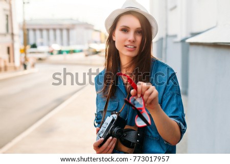 Summer closeup street portrait of young smiling beautiful and happy woman photographer posing with camera, wearing a hat