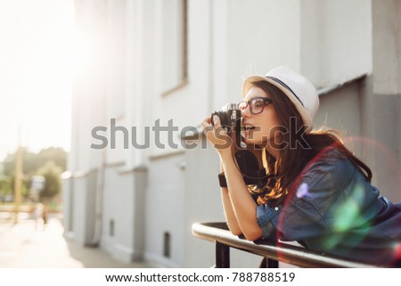 Summer closeup street portrait of young smiling beautiful and happy woman photographer posing with camera, wearing a hat