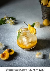 summer cocktail with apricot puree. there is a bucket of apricots in the back, there is a cut apricot and ice next to it on dark background