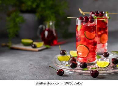 Summer cocktail in a clear glass with cherries, lime, peppermint and ice on a grey background. Mojito with cherries.