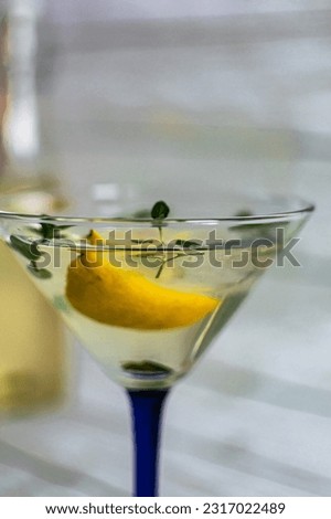 summer cocktail with lemon and mint in a transparent martini glass on a light background