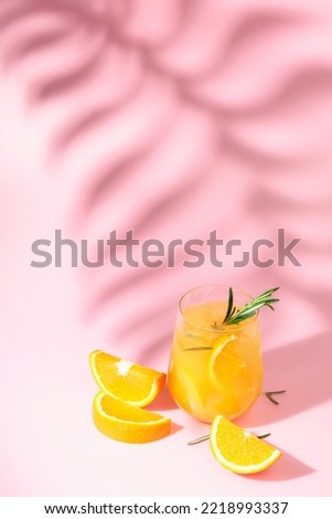 Summer cocktail with orange, rosemary, and ice. Drink on pink background with palm leaf shadow. Summer, tropical, fresh cocktail concept.