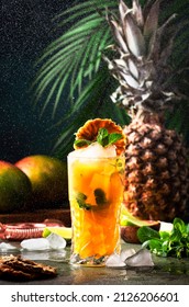 Summer Cocktail With Vodka, Pineapple Juice, Mango, Ice. Long Drink Or Cold Mocktail. Frozen Splashes And Flying Drops. Tropical Background With Palm Leaves 