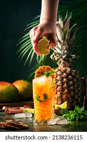 Summer cocktail with vodka, pineapple juice, mango, ice. Long drink or cold mocktail. Bartender hand squeezes lime juice, frozen motion and flying drops. Tropical background with palm leaves  - Shutterstock ID 2138236115
