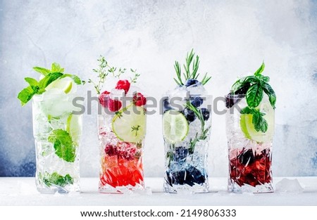 Summer cocktails or mocktails and cold drinks. Refreshing mojito drink with blueberries, blackberries, raspberries and  lime, herbs and ice on gray background