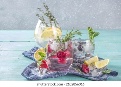Summer cold drink concept. Fruit and berries gin tonic cocktail, or infused water lemonade mocktails, with fresh blueberry, raspberry, lemon and herbs, blue green old wooden background copy space
