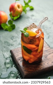 Summer cold drink, iced tea with nectarine or peach, ice and mint in a glass beaker on a green concrete background. Soft drinks, cold tea. Summer concept