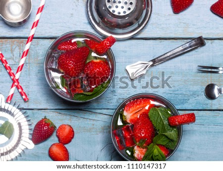 Summer cold drink with strawberries, mint and ice in glass on blue wooden background. Cocktail making bar tools with fresh berry fruits.