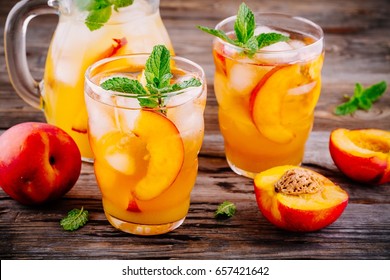Summer cold drinks: homemade peach sangria with ice cubes, and mint in glass on wooden background