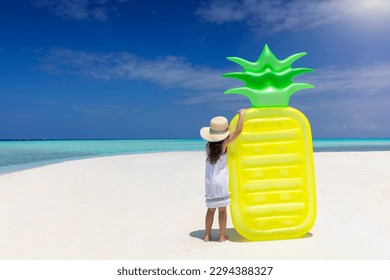 Summer concept with a little girl holding a pineapple shaped floaty on a tropical paradise beach