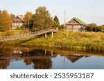 Summer country landscape at sunset. Old wooden houses and narrow suspension bridge over the Olonka River in the village of Verkhovye, Olonetsky district, Karelia