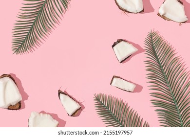 Summer creative layout with coconut pieces and palm leaves on pastel pink background. 80s or 90s retro aesthetic fashion background. Tropical fruit summer idea with copy space.