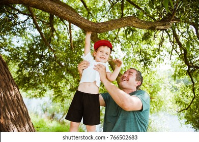 Summer. Dad Helps His Son Climb A Tree.