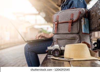 Summer day of Asian woman sitting using laptop at train station. She have camera film, Backpack, hat, map and smartphone. Travel and work freelance concept. hipster style.