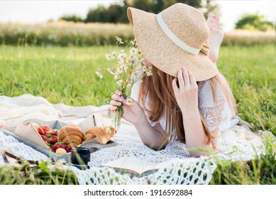 Summer day, picnic in the village. A beautiful girl in a hat lies on a plaid plaid. a bouquet of daisies, flowers in her hair.