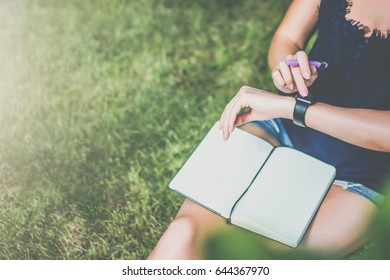 Summer day. View from above. Close-up of notepad lying on girl's lap.Girl sitting in garden on lawn under tree uses smartwatch and reading book, writes data to a notebook. Instagram filter. - Powered by Shutterstock