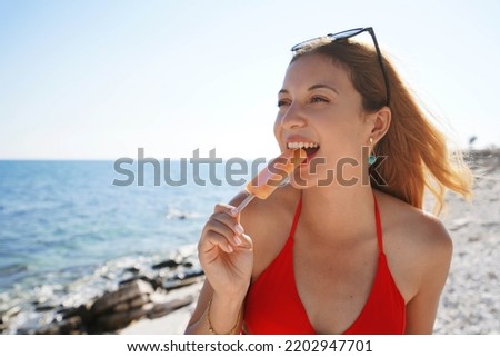 Summer days. Beautiful bikini woman biting a fresh popsicle on the beach.