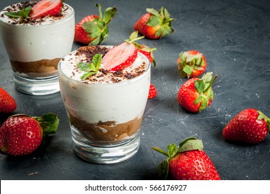 Summer dessert, classic cheesecake with strawberries decorated with mint leaves. On a dark gray stone or concrete table, copy space 