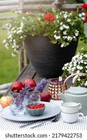 Summer Dinner Outdoor, Tea Party In The Garden With Cups, Porcelain Teapot, Apples, Currants And Flowers In Pot