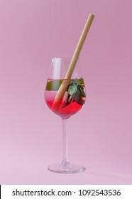 Summer drink with diffusing grenadine syrup, fresh mint leaves in a wineglass standing on a pastel pink background. It has an ecological bamboo straw in it.