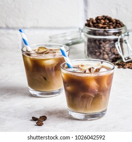 Summer drink iced coffee in glass and coffee beans in glass jar on white background. Selective focus, copy space. 