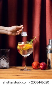 Summer Drink Making Or Chill Out  Concept, Woman's Hand Is Holding An Ice Cube To Add To Her Peach And Rosemary Gin Tonic Cocktail