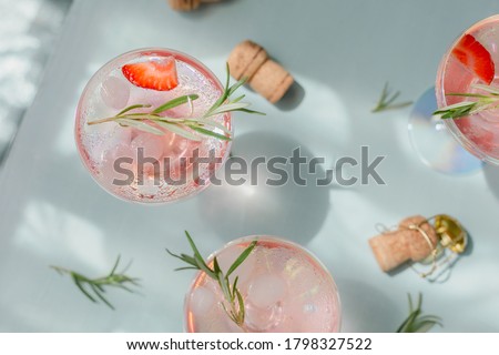 Summer drink with white sparkling wine. Homemade refreshing fruit cocktail or punch with champagne, strawberries, ice cubes and rosemary on light blue background.