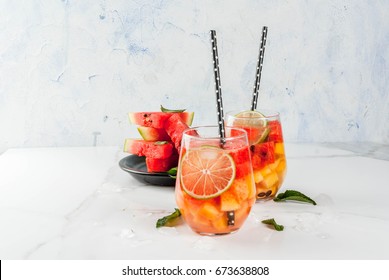 Summer drinks and cocktails. Lemonade, homemade sangria with fresh watermelon, lime, mint and pineapple. In two glasses,  on a white marble table. Copy space