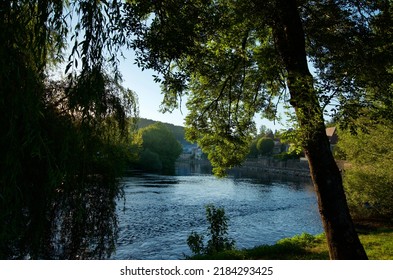 Summer Evening Light Overlooking The Vézère River And The Beautiful French Town Of Le Bugue, With Trees In The Foreground And Clear Skies. 