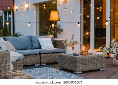 Summer Evening On The Terrace Of Beautiful Suburban House With Patio With Wicker Furniture And Lights