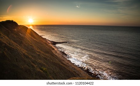 Summer evening sunset over the cliffs. Sea crashing up against the shore. Sun flares over the cliff top