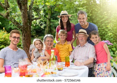 In Summer, Family Reunion Around A Picnic Table In A Beautiful Garden. All Generations Pose For The Camera. Shot With Flare