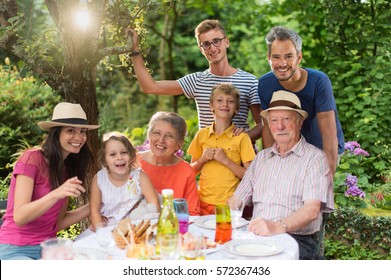 In summer, Family reunion around a picnic table in a beautiful garden. All generations pose for the camera. Shot with flare