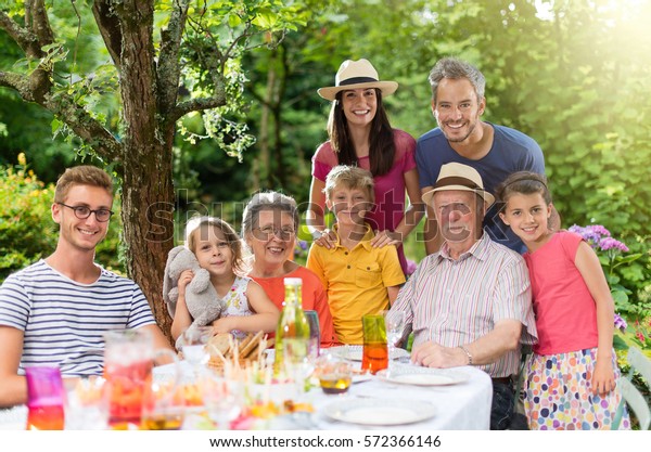 In\
summer, Family reunion around a picnic table in a beautiful garden.\
All generations pose for the camera. Shot with\
flare