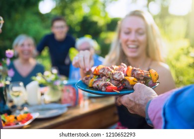 In the summer, a family of three generations gathered around a table in the garden to share a barbecue. close-up on a grilled meat dish presented to the guests - Powered by Shutterstock