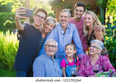 In The Summer, A Family Of Three Generations Gathered Around A Table In The Garden To Share A Meal. A Teenager Child Does A Selfie With All The Guests