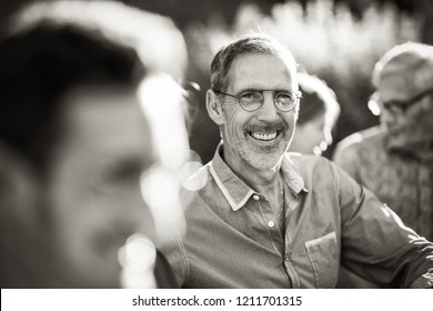 In The Summer, A Family Of Three Generations Gathered Around A Table In The Garden To Share A Bbq. Focus To A Handsome Man Looking At Camera. Black And White