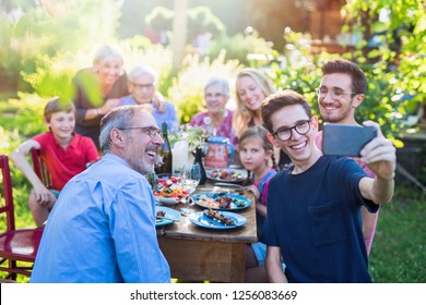 In The Summer, A Family Of Three Generations Gathered Around A Table In The Garden Sharing A Meal. A Teenager Does A Selfie With All The Guests