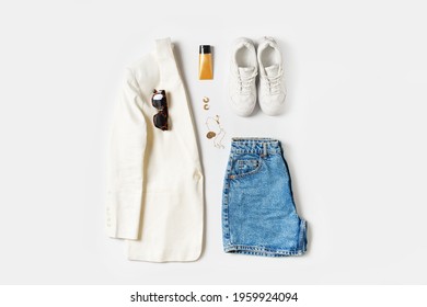 Summer fashion flat lay with white jacket, denim shorts, sunglasses, accessories and sneakers on white background, top view,