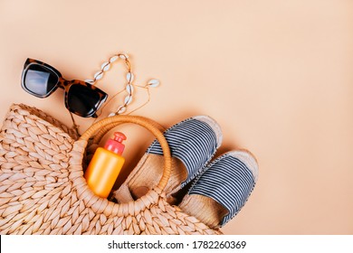 Summer Fashion Flatlay With Summer Straw Bag, Striped Espadrilles Sandals, Sea Shell Necklace, Sunscreen And Tortoiseshell Sunglasses Isolated On Beige Background.